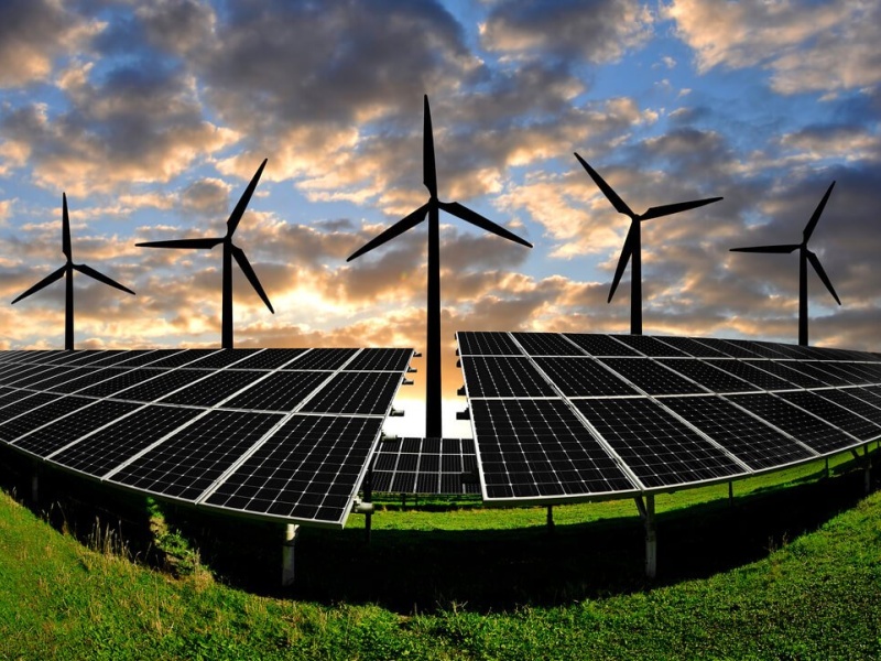 solar panels and wind turbines against a sunset sky
